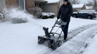 Person using a snow blower on a snow-covered driveway.