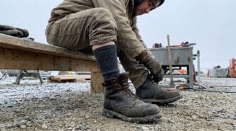 Worker tying sturdy boots on a construction site with cold, rocky ground.