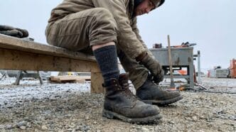 Worker tying sturdy boots on a construction site with cold, rocky ground.